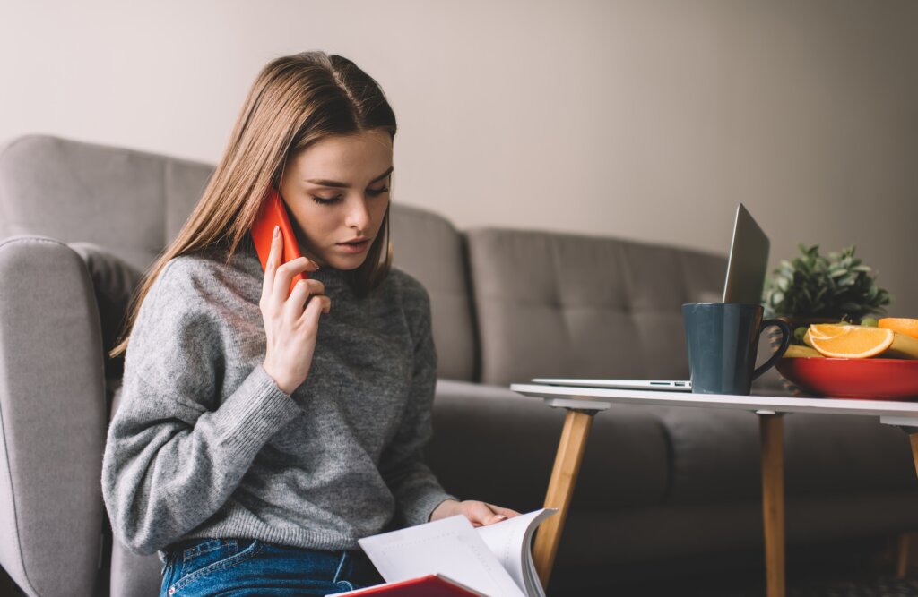 Focused young woman talking on phone and flipping copybook